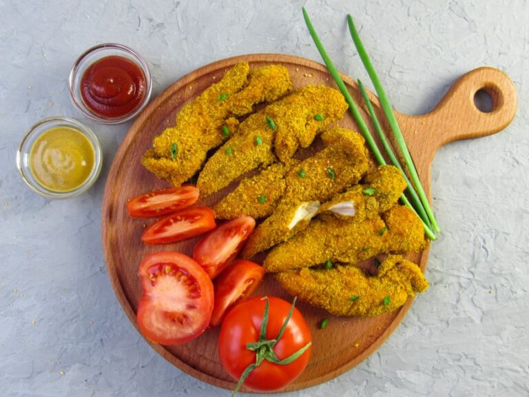 Crispy chicken fingers served with ketchup, mustard, and sliced tomatoes on a wooden tray.