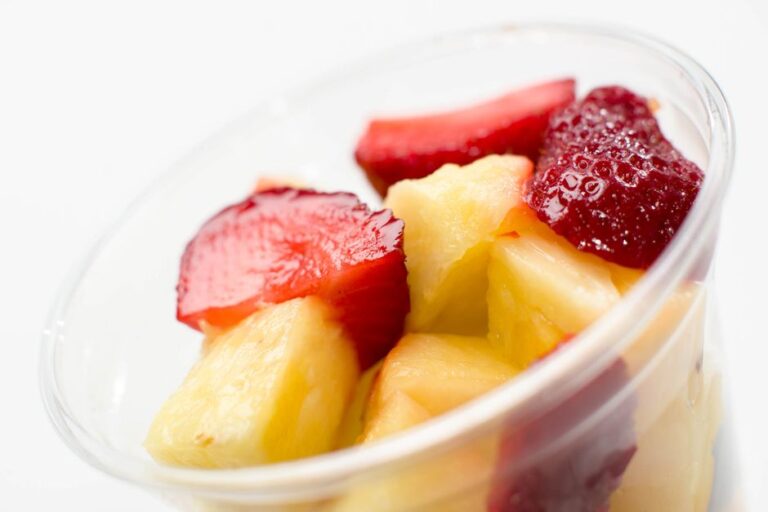 Close-up of fresh fruit salad in a clear cup featuring sliced strawberries and pineapple.