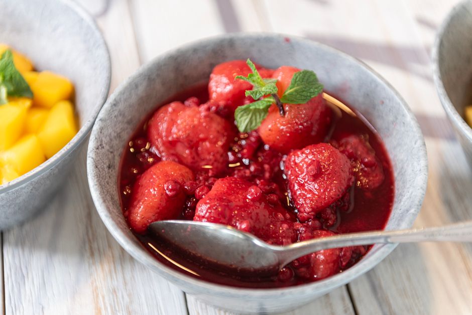 Bowl of fresh strawberries in a luscious syrup, garnished with mint leaves.